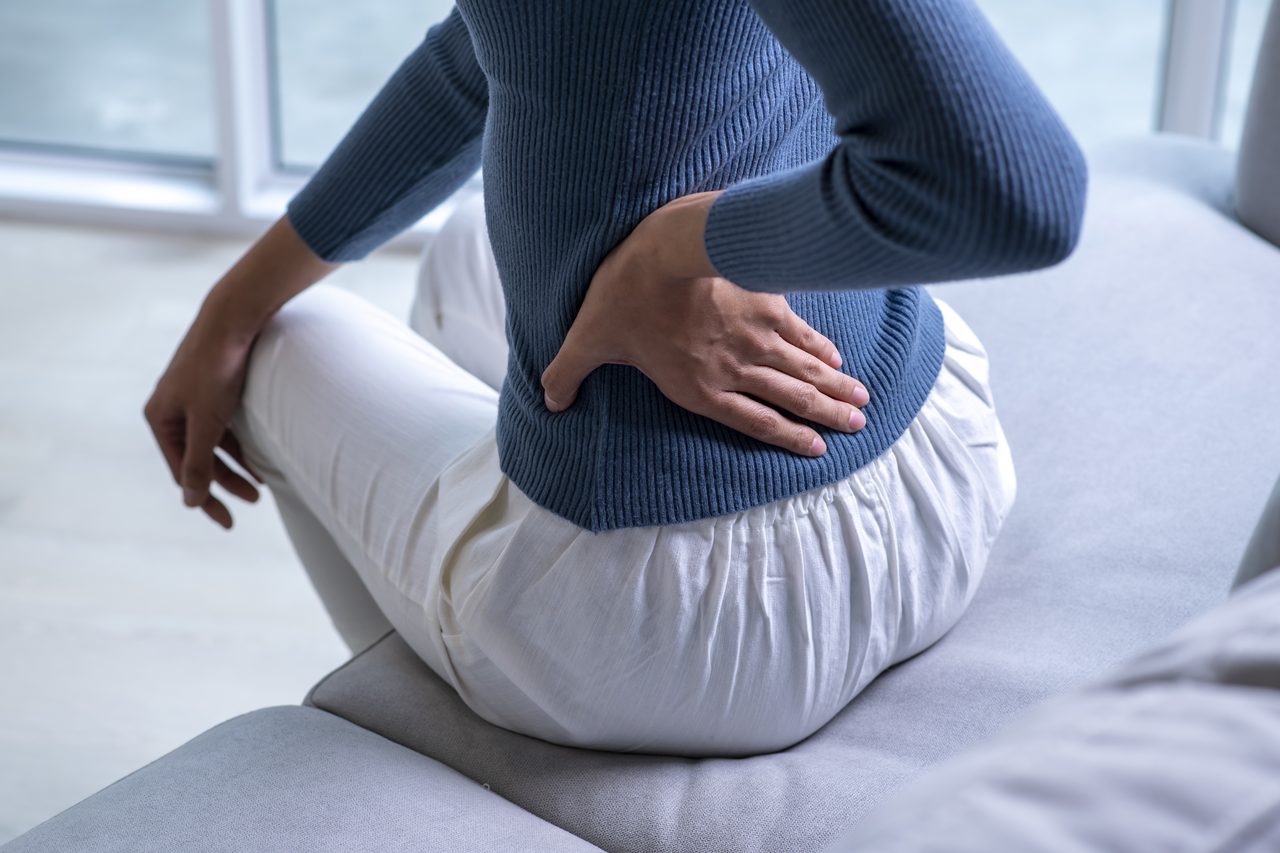 A woman seated on a couch holding her lower back.
