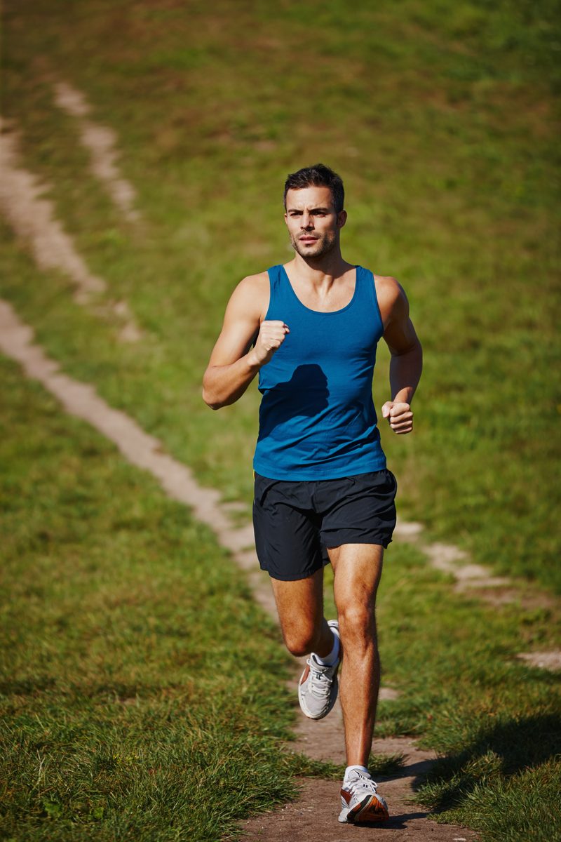 A focused man running on a grassy trail.